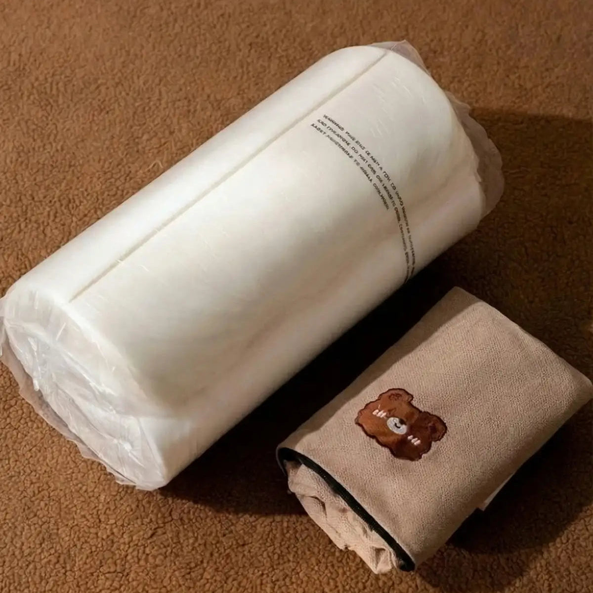 Vue du produit à la livraison : rouleau de mousse blanche comprimée sous plastique et housse en tissu beige pliée à côté.