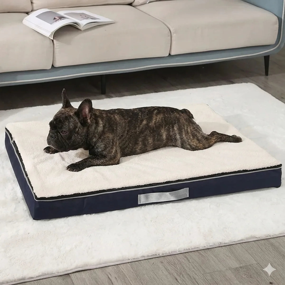 Bouledogue français bringé allongé confortablement sur le lit orthopédique à mémoire de forme bleu marine. La surface en mouton blanc offre un soutien optimal pour ses articulations.